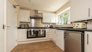 A modern kitchen with white cabinets, a stainless steel range hood, a dishwasher, and a built-in oven. - Budget-Friendly Group Stay in Newport - Pass the Keys (Newport)