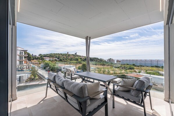 Ein Balkon mit Tisch und zwei Sofas, mit Blick auf eine Wohngegend mit Gebäuden und Grünflächen.