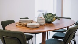 Una mesa de madera redonda con individuales tejidos, platos apilados y un bol de verduras.
