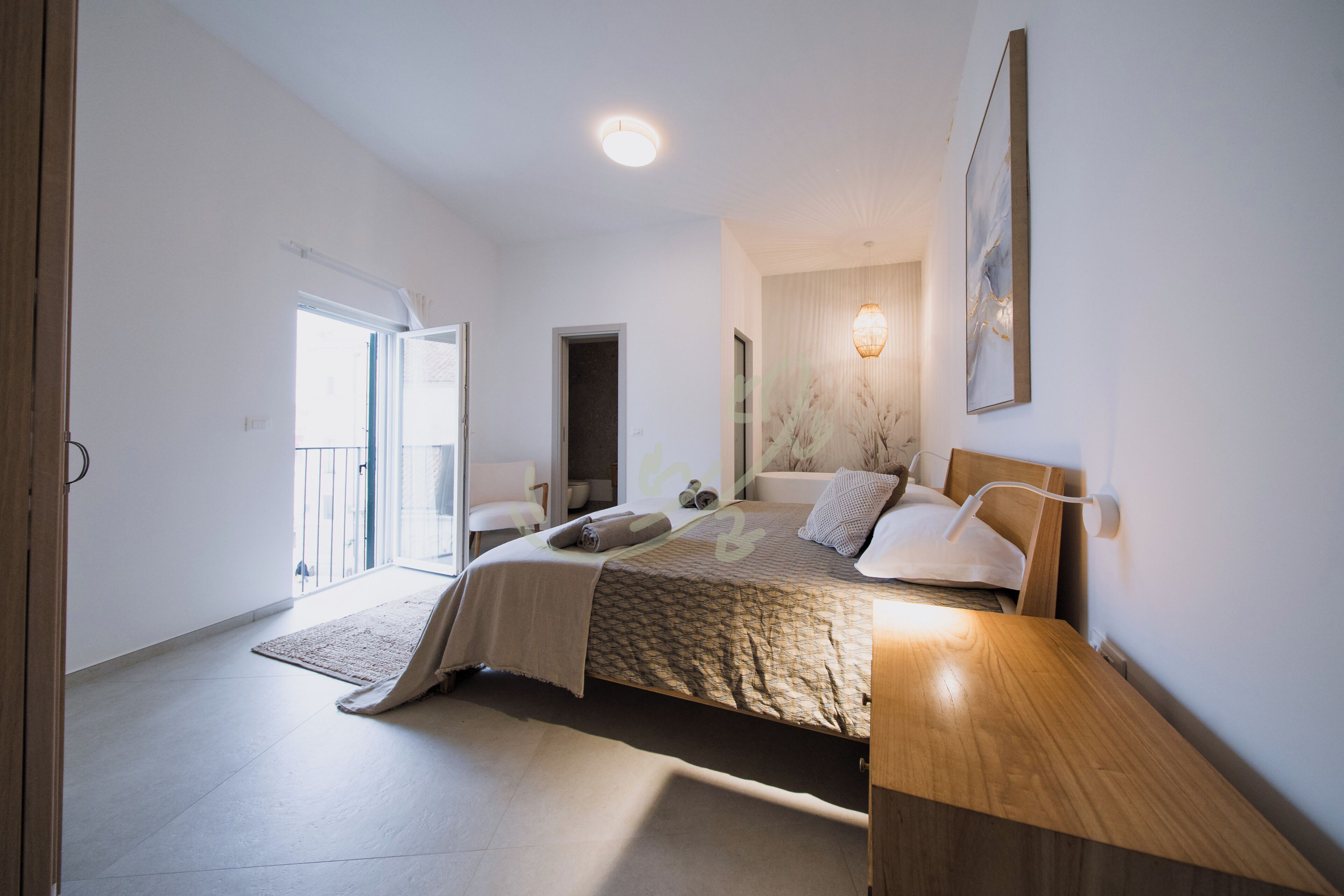 Ein Schlafzimmer mit Bett, Nachttischen, einer Wandlampe und einer Tür zu einem anderen Raum.