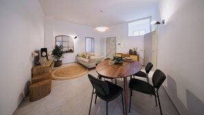 Una sala de estar moderna con una mesa de comedor redonda de madera, sillas negras, un sofá beige, una escalera de madera y un ventanal grande.