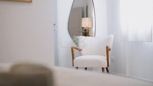 Un sillón blanco con patas de madera, un espejo ovalado grande en la pared y una puerta con interruptor de luz.