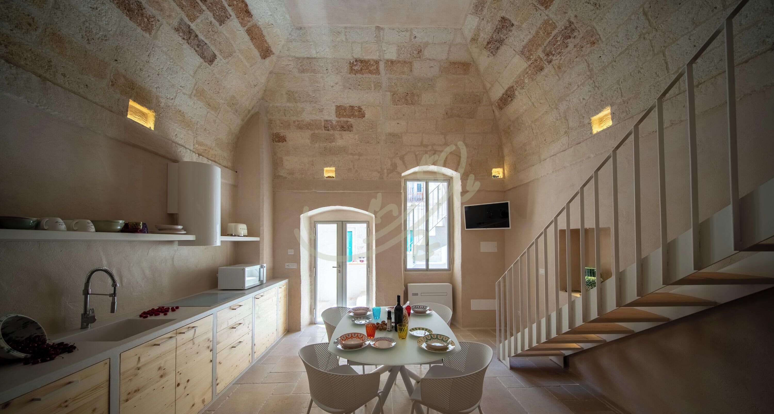 A narrow kitchen with a dining area, a staircase, and a TV mounted on the wall.