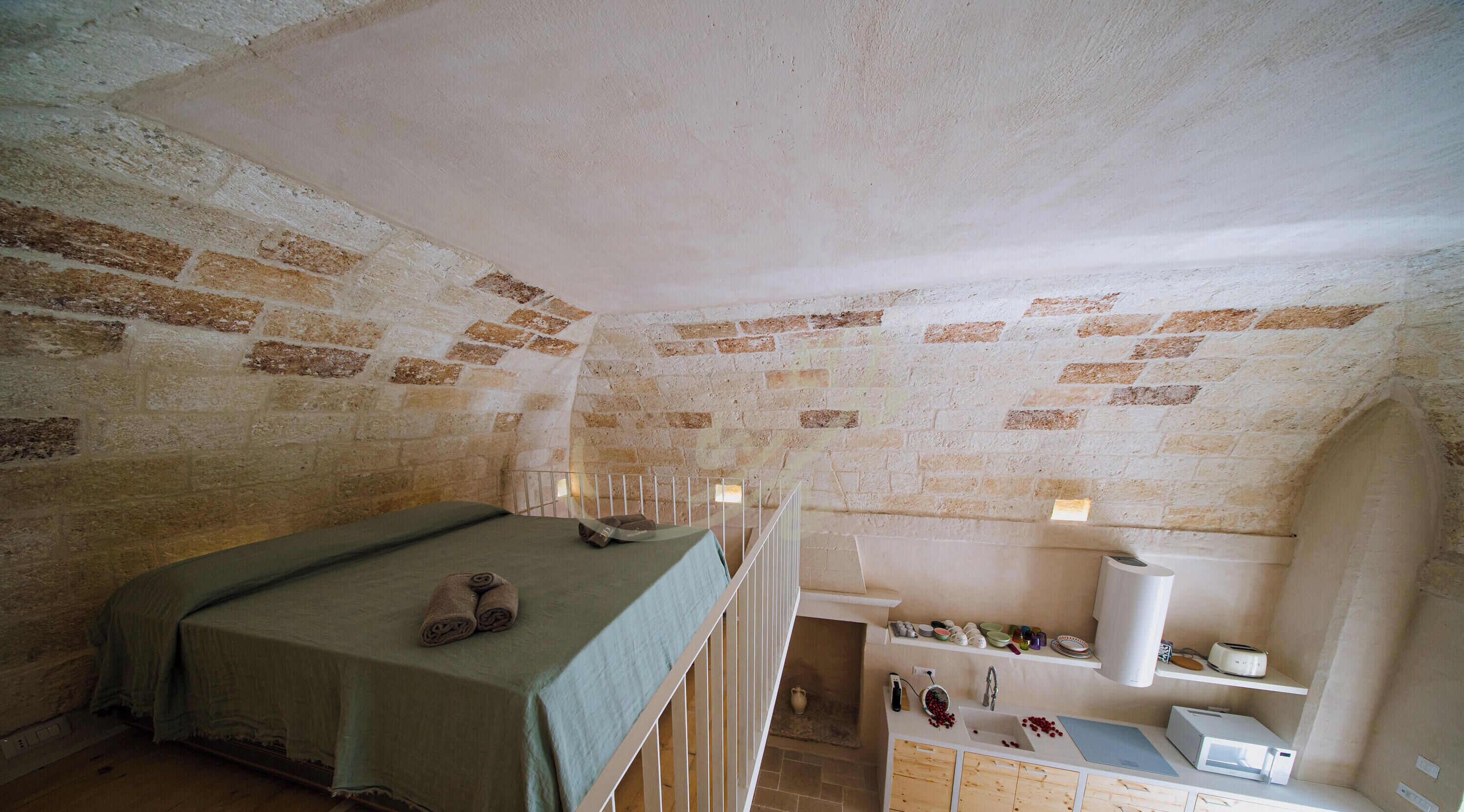 Ein Zimmer mit einem Bett, einer kleinen Küchenzeile und einer Backsteinwand.