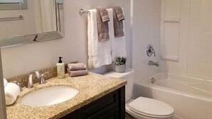 Un baño con lavamanos, espejo, toallero, inodoro y bañera.