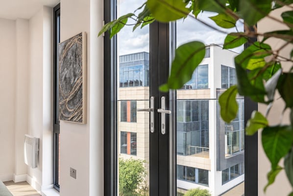 Ein modernes Interieur mit einem großen Fenster, einem Wandbild und Blick auf ein zeitgenössisches Gebäude.