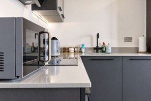 Moderni keittiö, jossa on sisäänrakennettu liesi, kahvinkeitin ja erilaisia keittiötarvikkeita työtasolla.