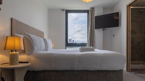 Quarto de hotel moderno com uma cama grande, abajur, TV de tela plana e vista para a cidade.