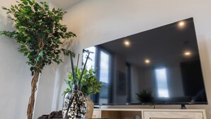 Uma sala de estar moderna com televisão de tela plana, uma mesa de madeira, uma planta em vaso e um vaso com folhagem.