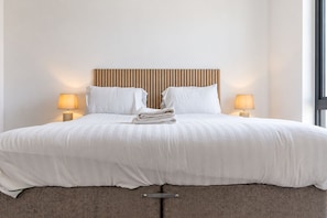 Ein Hotelzimmer mit einem Bett, zwei Nachttischlampen, einem Kopfteil und einem Fenster.