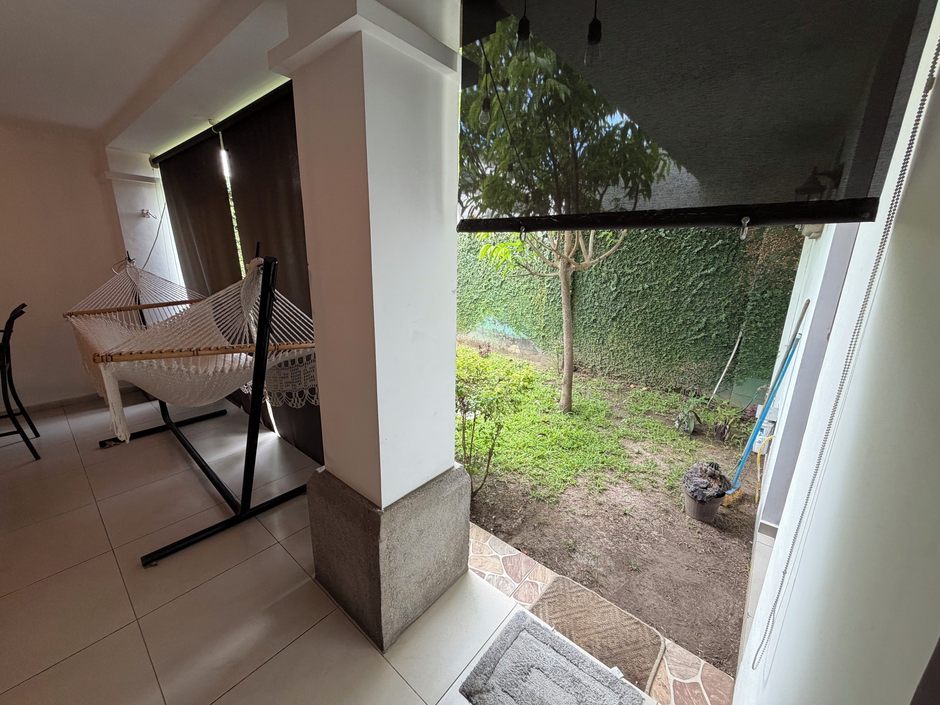A room with a hammock chair, a view of a garden, and a sliding door leading outside.