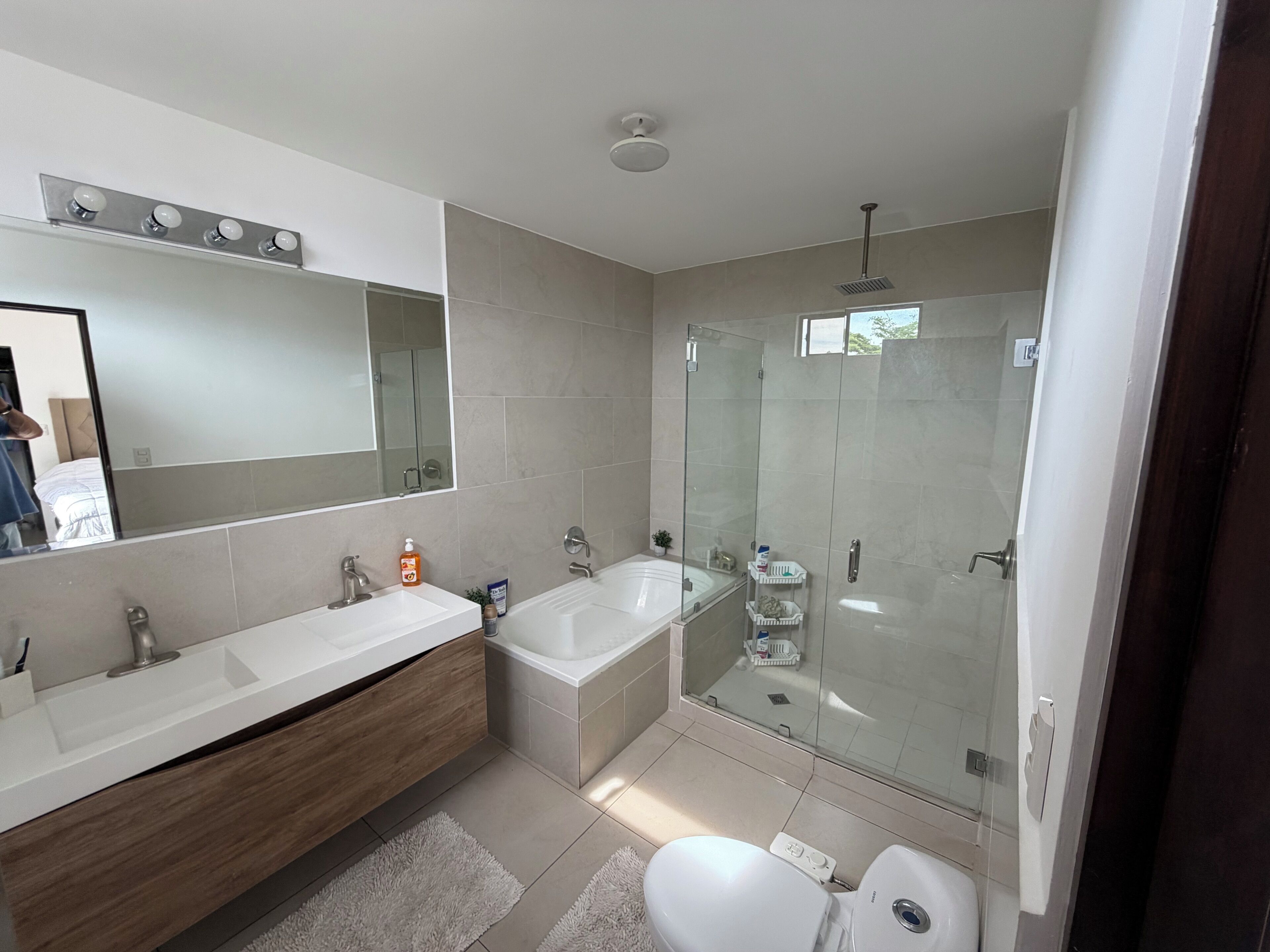 A modern bathroom with a large mirror, a double sink vanity, a bathtub, and a glass-enclosed shower area.