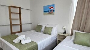 Habitación de hotel con dos camas, una escalera de madera, un cuadro con sillas de playa y una mesita de noche con lámpara.