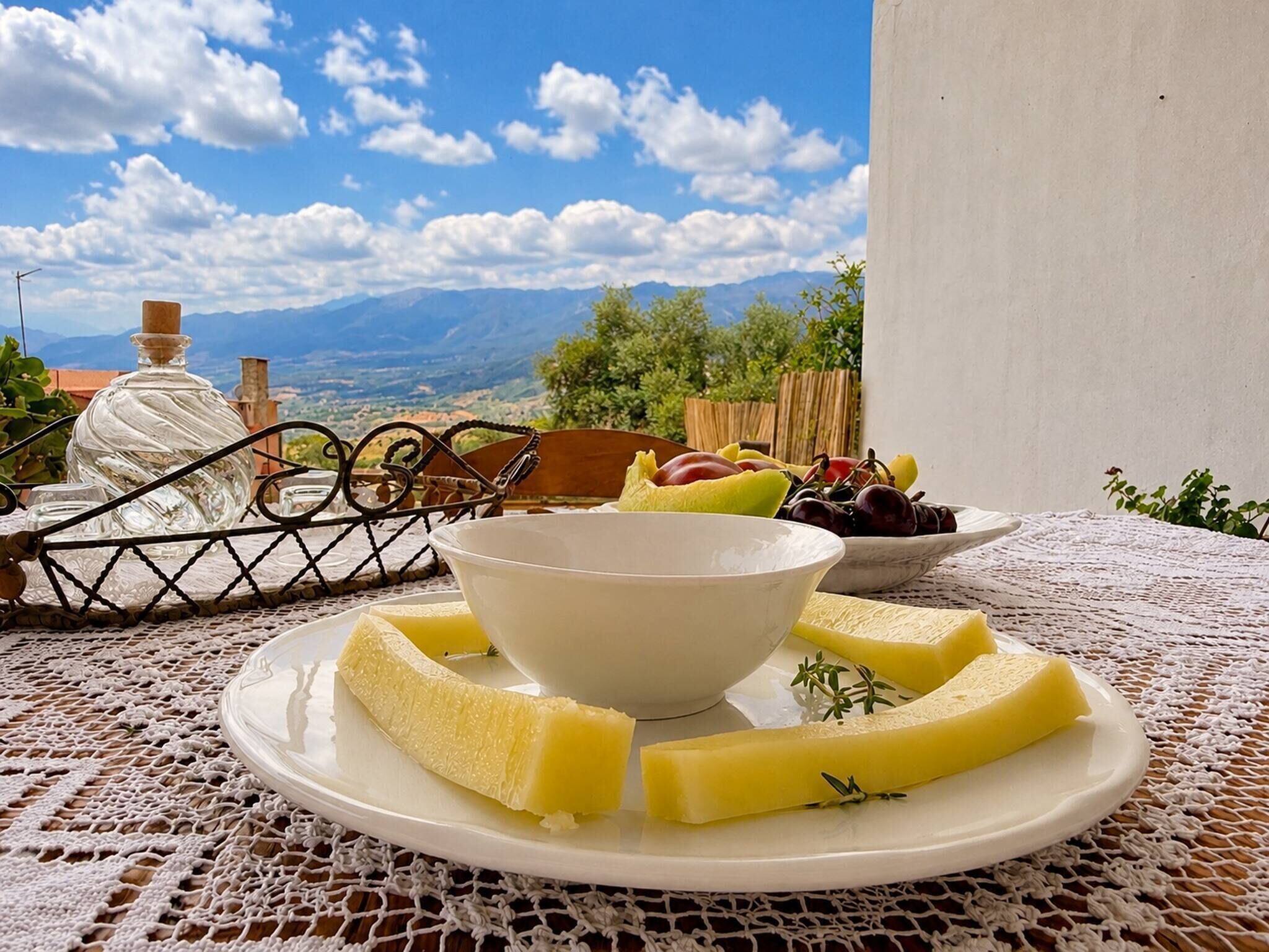 A table with a white bowl, a plate with cheese slices, and a bowl of fruit.