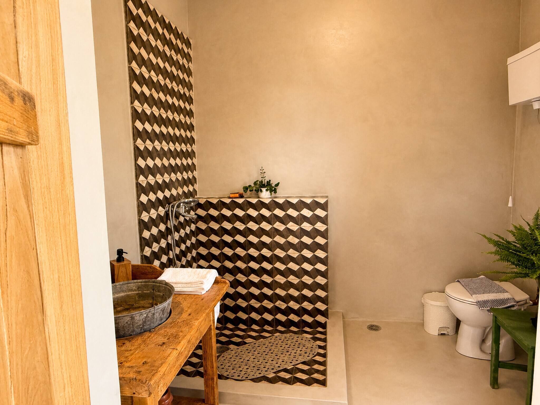 Ein Badezimmer mit einer Dusche, deren Wand ein geometrisches Muster aufweist, einem Holztisch mit einer Schüssel, einem Waschbecken und einer Toilette.