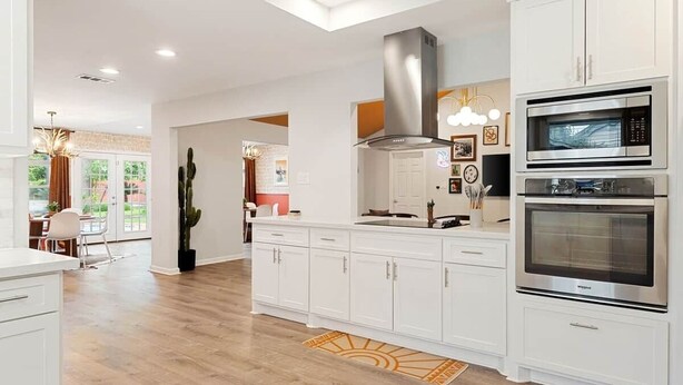 Una cocina moderna con armarios blancos, una campana extractora de acero inoxidable y dos hornos integrados.