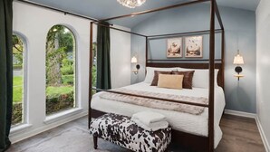 Una cama con dosel con vistas a un jardín a través de ventanales arqueados, un candelabro y lámparas de pared.