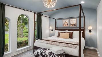 Uma cama com dossel e vista para um jardim através de janelas em arco, um candelabro e luminárias fixadas na parede.