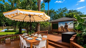 Una terraza de madera con una mesa, sillas, una sombrilla y una parrilla.