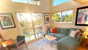 A living room with a sofa, a coffee table, and a chair. There are windows with a view of trees and a balcony. - Panoramic views on Beacon Hill, Seattle (Seattle)