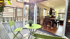 Une terrasse ouverte avec une table et des chaises, un pot de fleurs et une vue sur un coin repas équipé d’une table et de chaises.