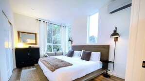 A modern bedroom with a large bed, a dresser, a mirror, and a window with curtains. - Capitol Hill private terrace & mountain views (Seattle)