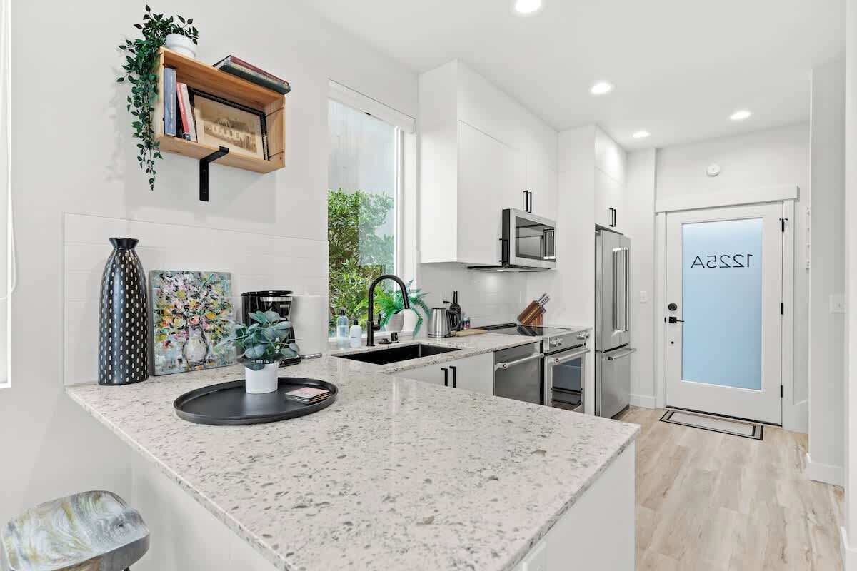 A modern kitchen with white cabinetry, a granite countertop, and a door with 'ASSA' visible.