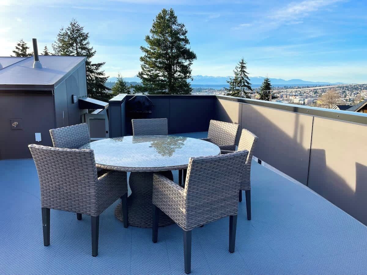 Ein runder Tisch mit Korbstühlen auf einer Dachterrassen-Sitzecke mit Blick auf Stadt und Berge.
