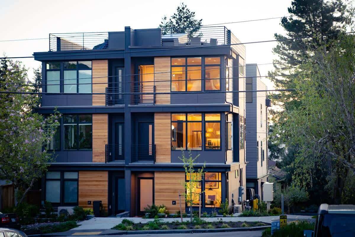 A modern multi-story residential building with large windows, a balcony, and a well-maintained garden.