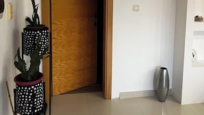 Huone, jossa on puinen ovi, ruukussa oleva kasvi, metallinen roskakori ja laatoitettu lattia.