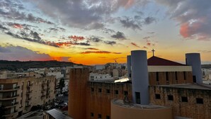 A cityscape with buildings, a church with a cross, and a sunset sky. - Comfy 1 bedroom apartment in Qawra (St Pauls bay)