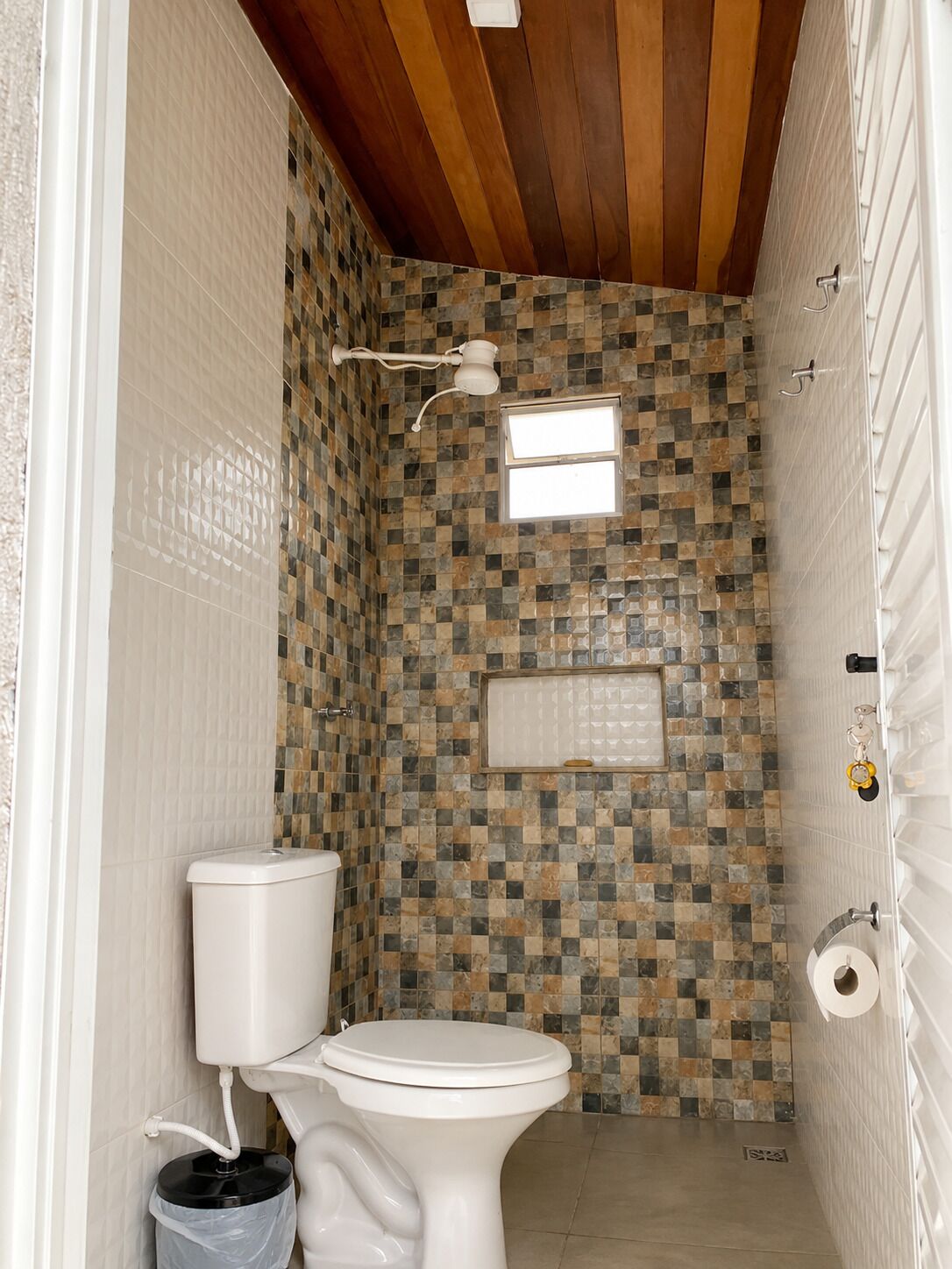 Une petite salle de bain avec un mur carrelé, des toilettes, une fenêtre et un porte-serviettes.