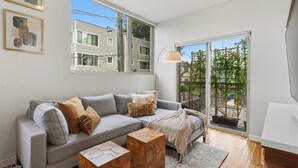 A modern living room with a grey sofa, wooden coffee table, and a large window with a view of a residential area. - Spacious Townhome in an Unbeatable Location (Seattle)