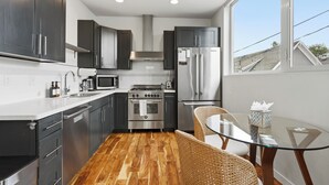 A modern kitchen with dark cabinets, stainless steel appliances, a glass dining table, and a view of the outside. - Spacious Townhome in an Unbeatable Location (Seattle)