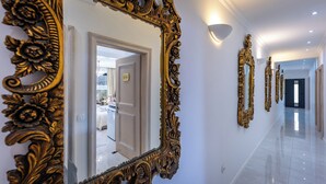 Um corredor com espelhos dourados elaborados, um lustre e uma porta que dá para um quarto.