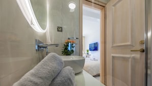 Uma casa de banho com uma pia branca, uma toalha, um vaso com flores e uma porta.