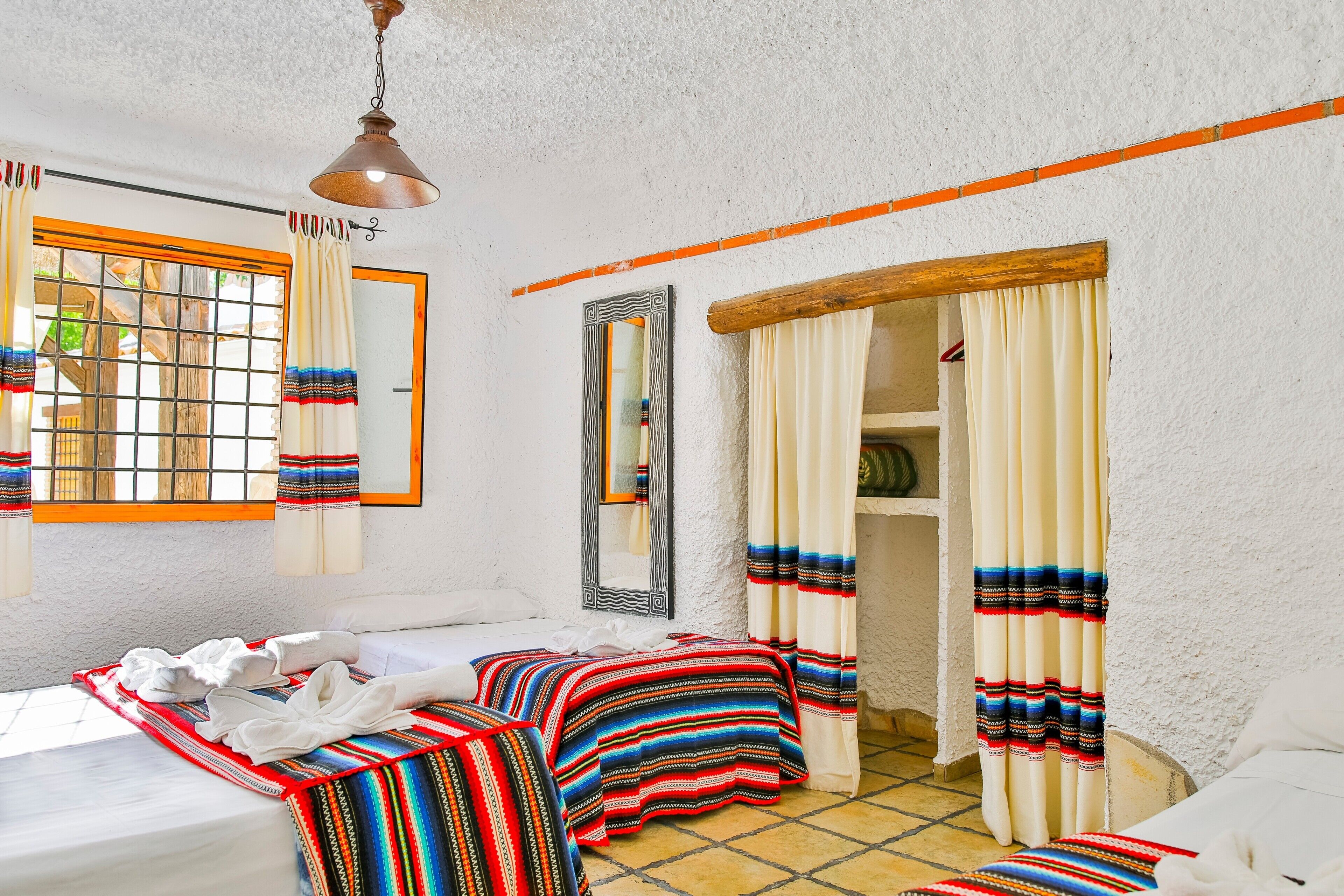 A room with a bed, a window with curtains, a mirror, and a door.