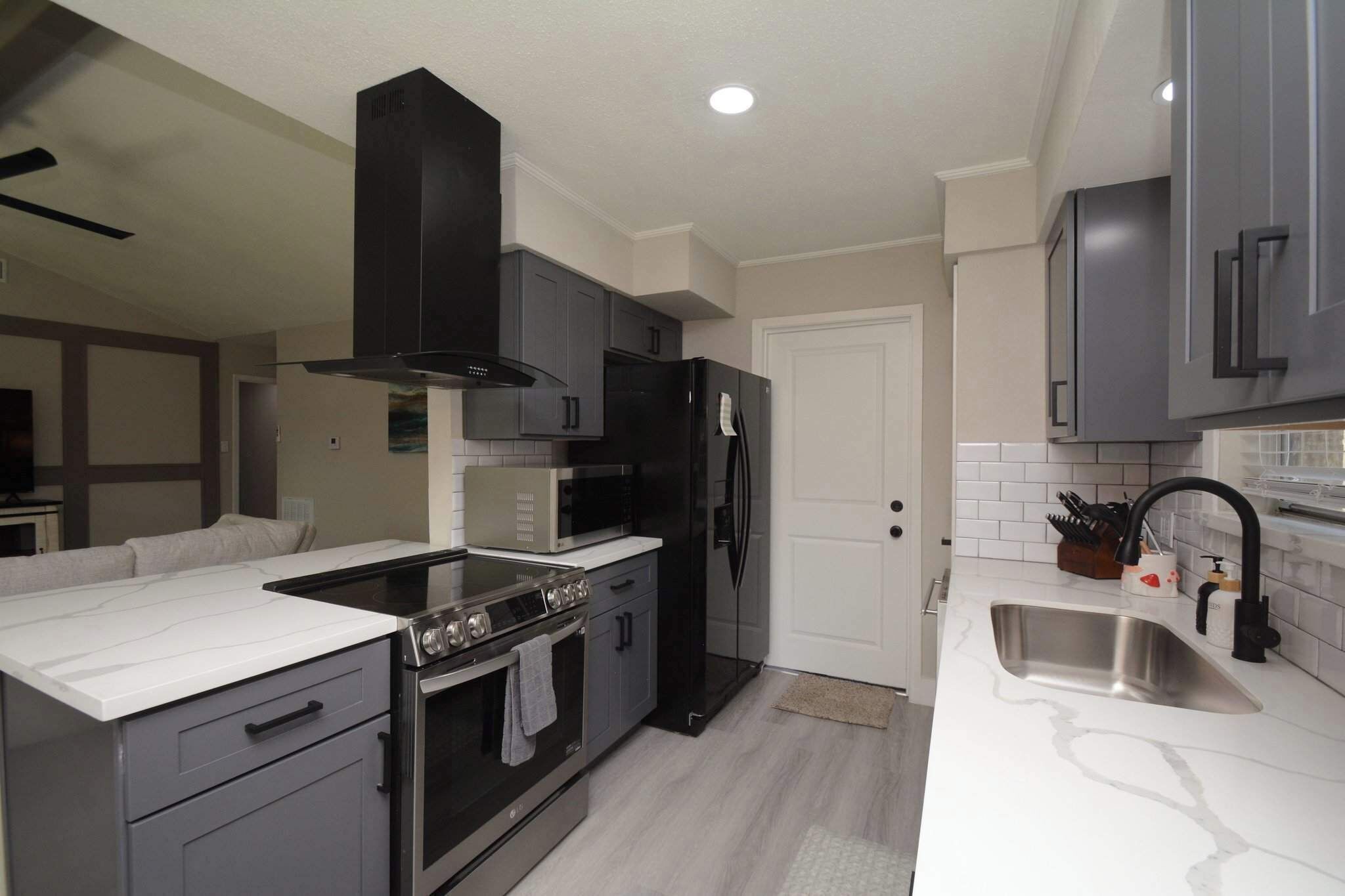 A modern kitchen with grey cabinets, a black range hood, a stainless steel sink, and a white countertop.