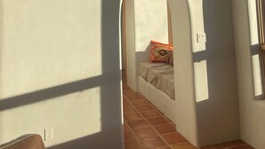 Ett rum med ett sluttande tak, ett litet fönster, en säng med en färgglad kudde och ett klinkergolv.