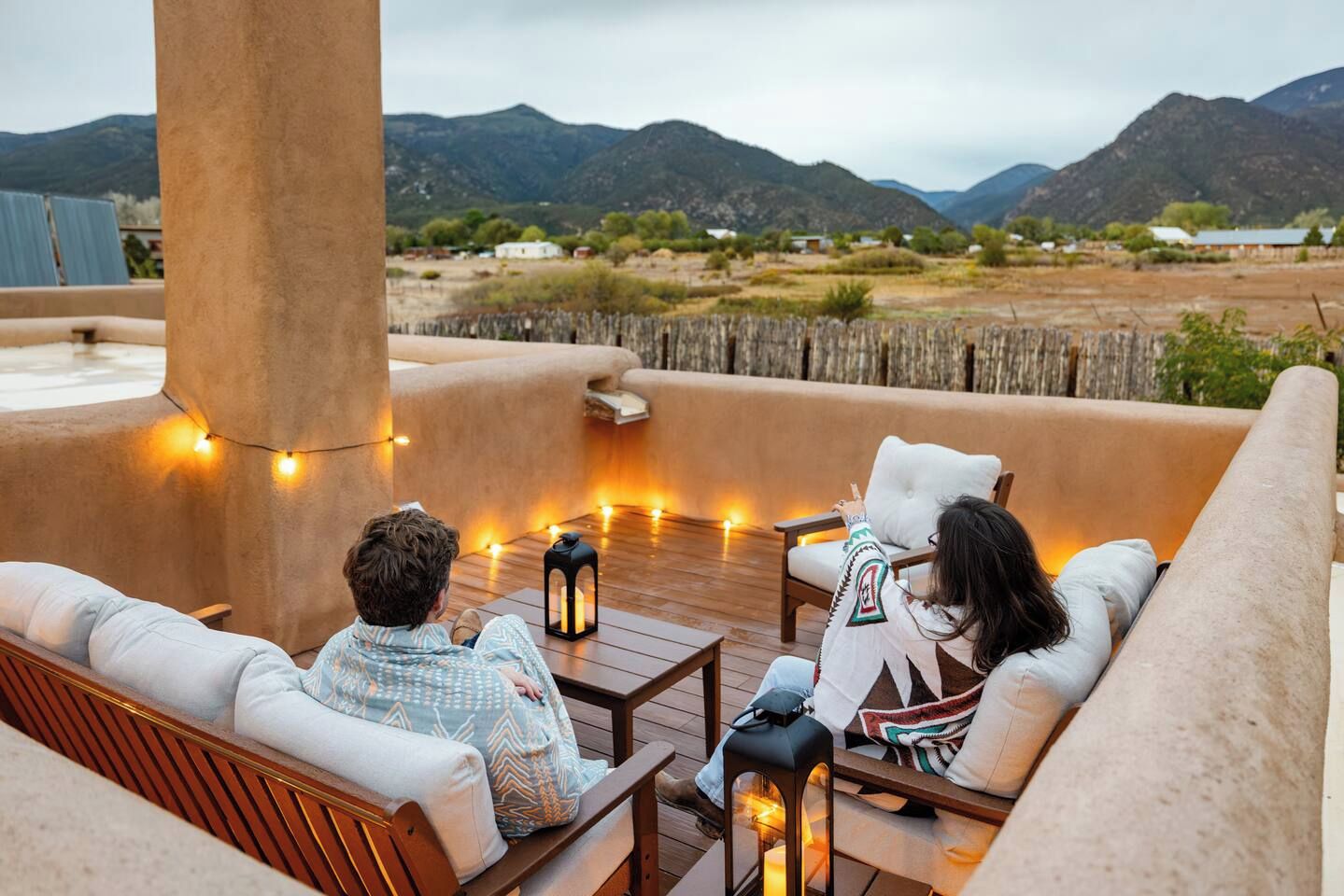 A rooftop terrace with seating and string lights, overlooking a mountainous landscape.
