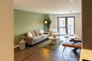 A modern living room with a sofa, armchair, coffee table, and a dining area with chairs and a table. - Modern York Apartment - Free Parking - Sleeps 7 (York)
