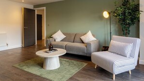 A living room with a sofa, armchair, coffee table, and a floor lamp. - Modern York Apartment - Free Parking - Sleeps 7 (York)