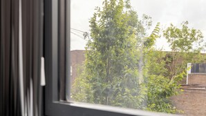 A window with a view of a brick wall and green foliage. - Modern York Apartment - Free Parking - Sleeps 7 (York)