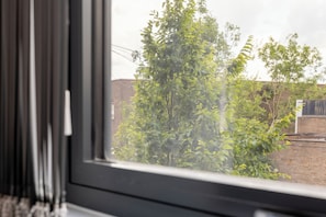 A window with a view of a brick wall and green foliage. - Modern York Apartment - Free Parking - Sleeps 7 (York)