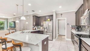 Une cuisine moderne dotée d’un îlot en marbre, de meubles en bois foncé, d’appareils électroménagers en acier inoxydable et de luminaires suspendus.