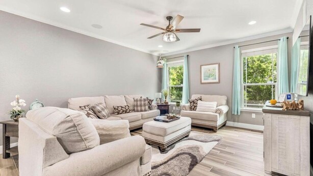 Un salon comprenant un canapé, un fauteuil, un pouf et un ventilateur de plafond.