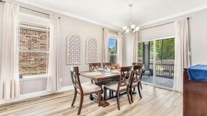 Un espace repas avec une table et des chaises en bois, un lustre et une vue sur l’extérieur.