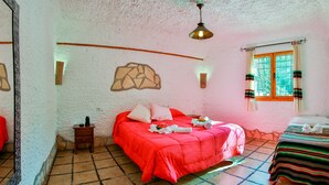 A room with a red bed, a small bedside table, a wall-mounted light fixture, and a window with curtains.