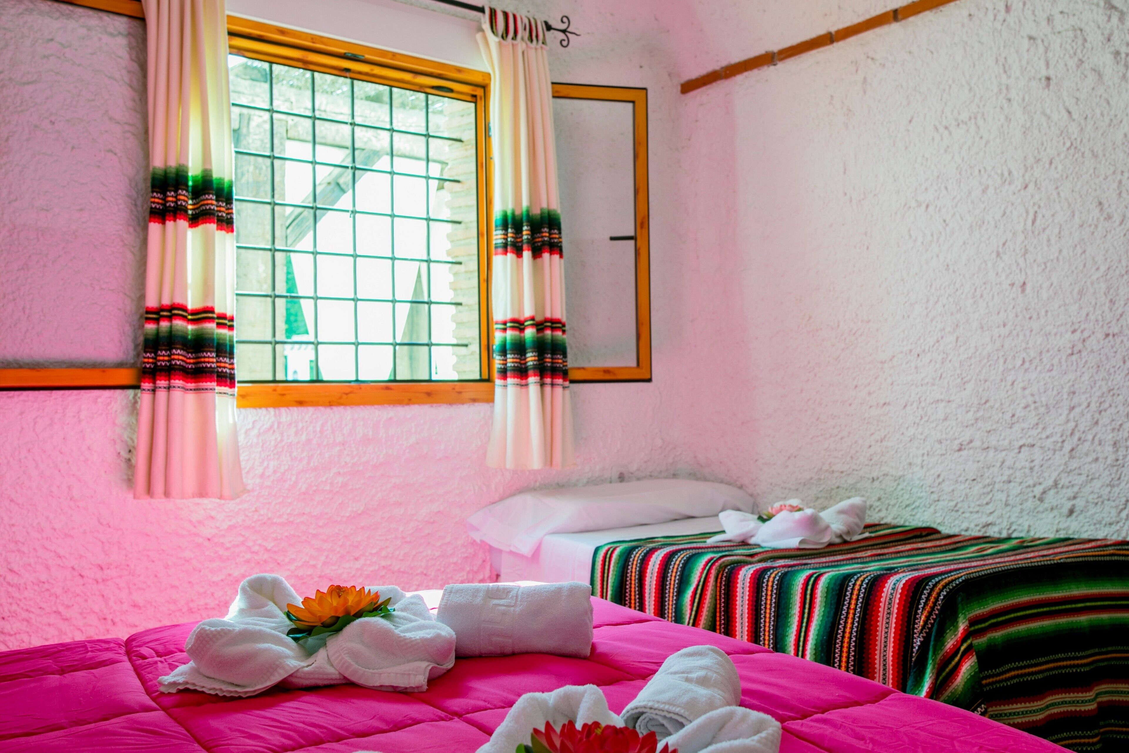Una habitación con dos camas, una ventana con cortinas y un espejo en la pared.
