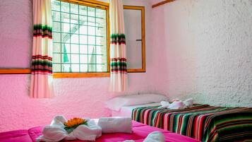 Una habitación con dos camas, una ventana con cortinas y un espejo en la pared.